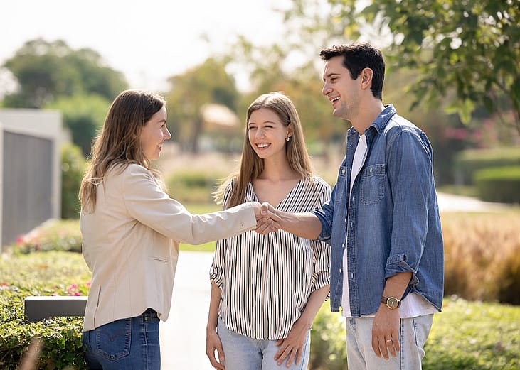 Happy young couple and real estate insurance agent shaking hands outdoors.