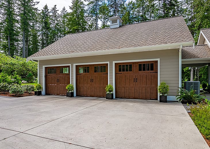 A craftsman style home with a three-car garage with lush and spring foliage landscape outside.