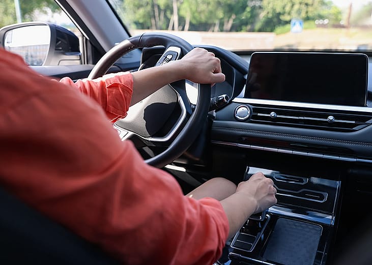 A person driving behind the steering wheel of a modern car.