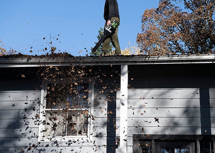 A cleaner removing leaves and debris from the gutter of a home's roof on a fall day.