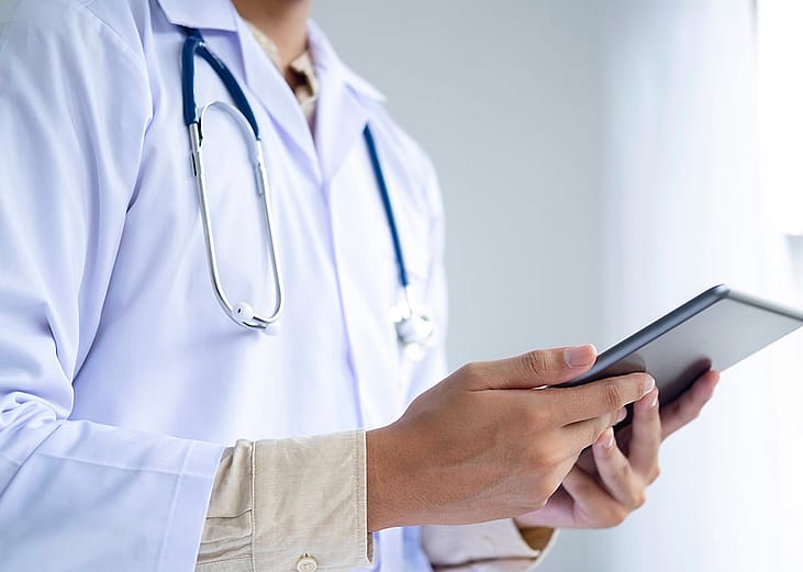 A medical doctor holding a digital tablet with patients' charts in a clinic.