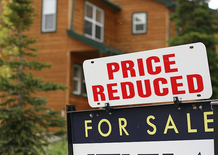 A For Sale sign with a Price Reduced sticker displayed in front of a residential house.