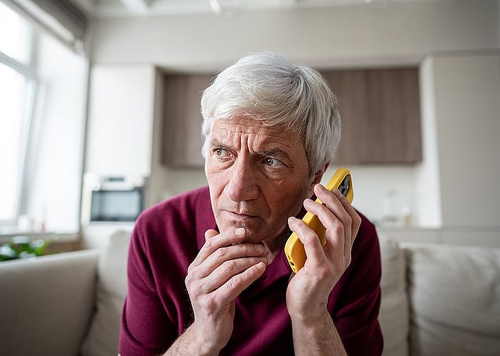 An elderly person listening over the phone to an unknown caller making dubious requests.