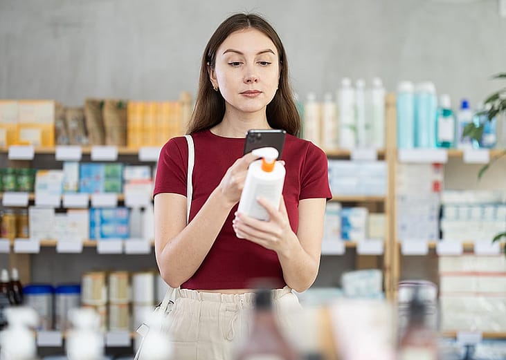 A young adult scanning the QR code of a moisturizing cream for sale inside a skincare shop.