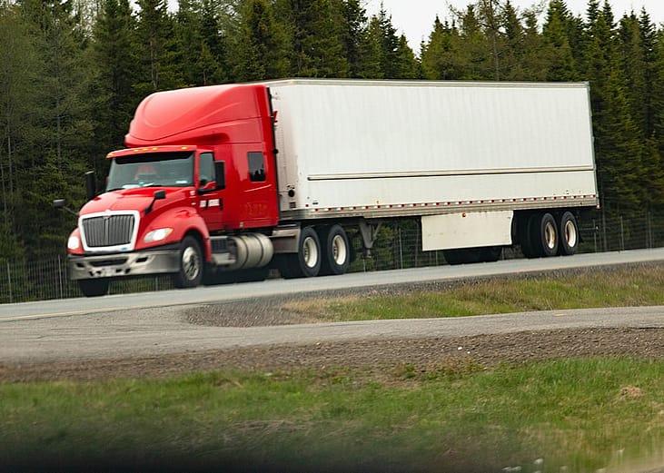 A truck carrying cargo loads while slowing down the hill during daytime.