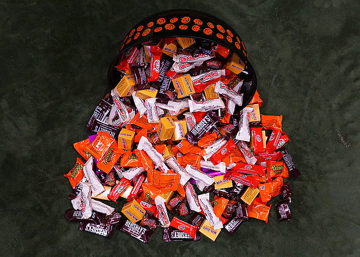 A variety of chocolates and candies spilling from a Halloween basket onto a flat surface.