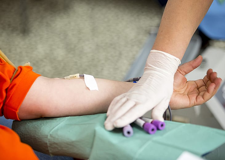 A person donating blood and a nurse holding blood collection tubes in a mobile blood donation center.