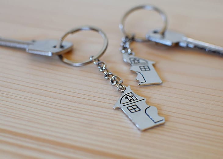 Two keys with divided house pendants on a wooden floor, representing a concept of division of shared property.