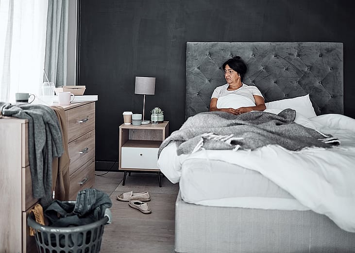 An elderly person feeling sad and zoning out in her unorganized bedroom alone.