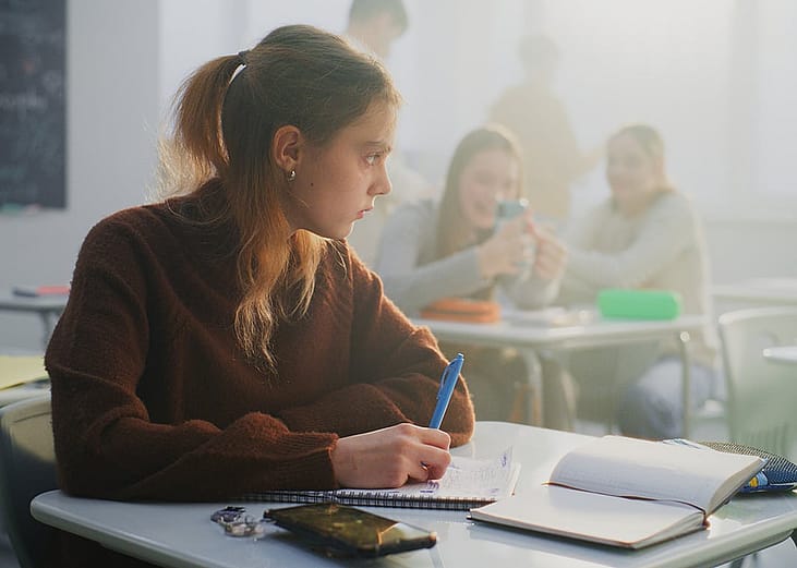 A teen student isolating herself from other students socializing with each other in the classroom.