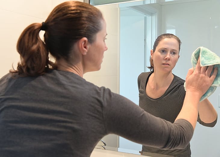 A person cleaning a large mirror at their home bathroom.