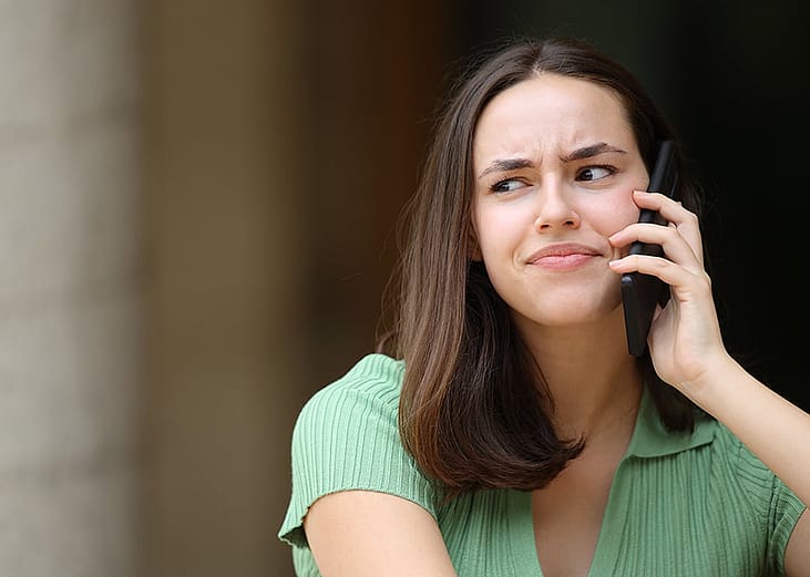 A person looking unconvinced while talking to a potential scammer over the phone.