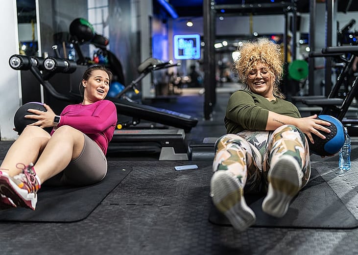 Friends holding exercise balls and bonding over workouts in the gym.