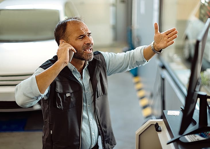A frustrated mechanic making a phone call at an auto repair shop.