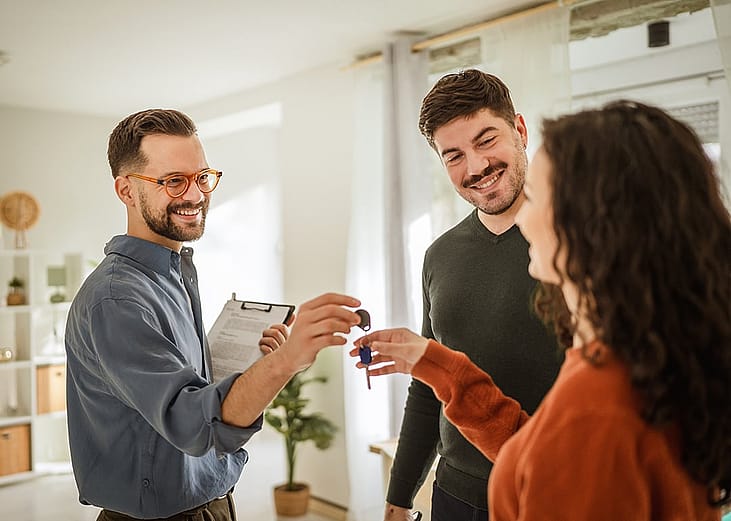 A landlord handing house keys to a newly married couple of their apartment.