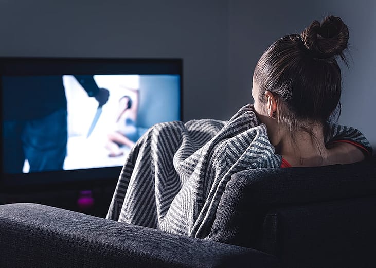 A woman at home watching a horror movie on the television.