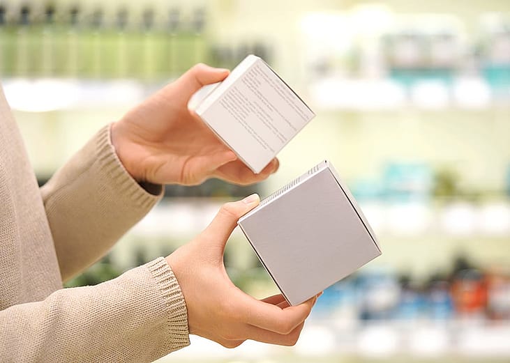 A shopper comparing the ingredient labels of two cosmetic products inside a beauty store.
