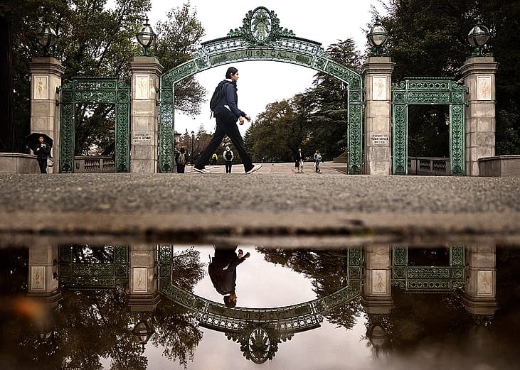 A student is reflected in a rain puddle while passing by Sather Gate at the University of California, Berkeley.