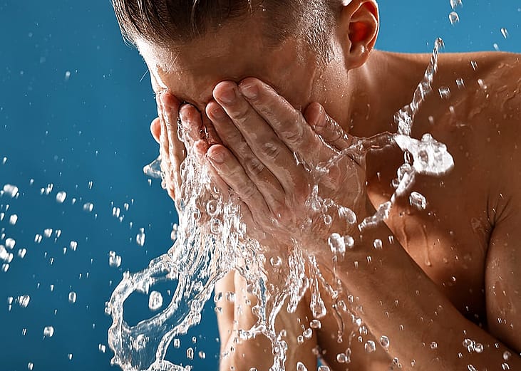 A man splashing water on his face against a blue background.