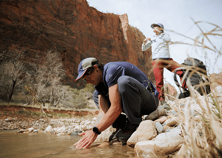 A hiker rinses his hands kneeling by a stream.