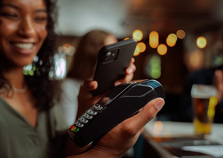 A person tapping her smartphone to a card machine for her digital payment in a bar restaurant.