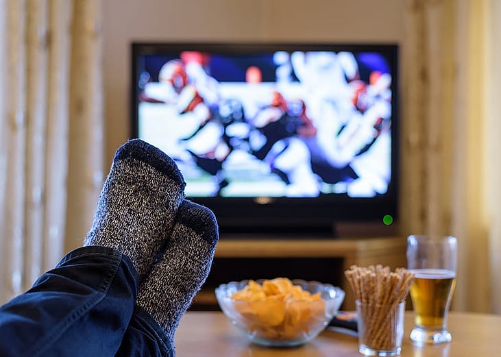 A man's feet on a table while watching a football match on a television.