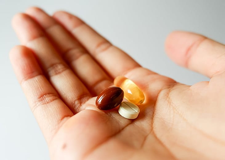 Different vitamin tablets seen on a person's hand.