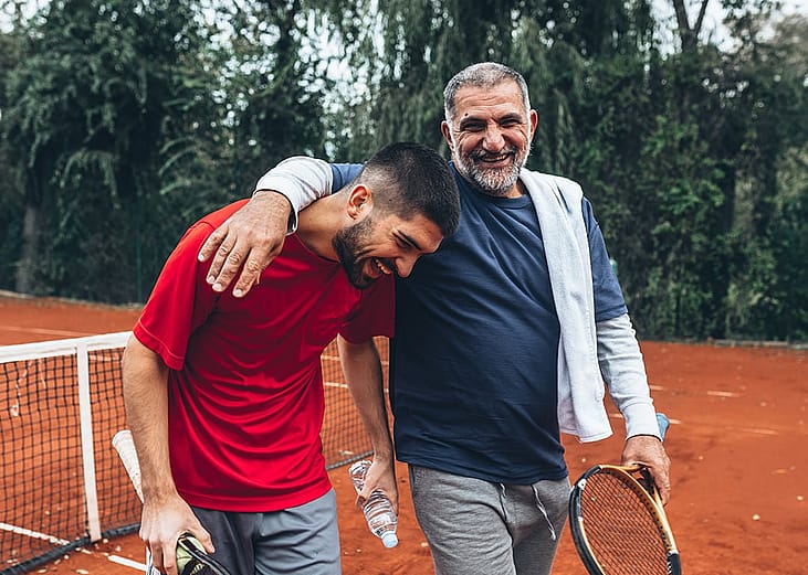 A father and son sharing a laugh after playing tennis in the court.