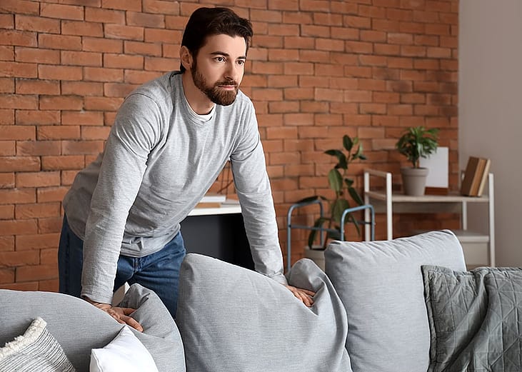 A person pausing and contemplating in thought over a couch in the living room.