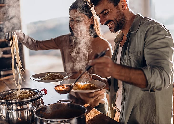 A couple cooking pasta together at home.