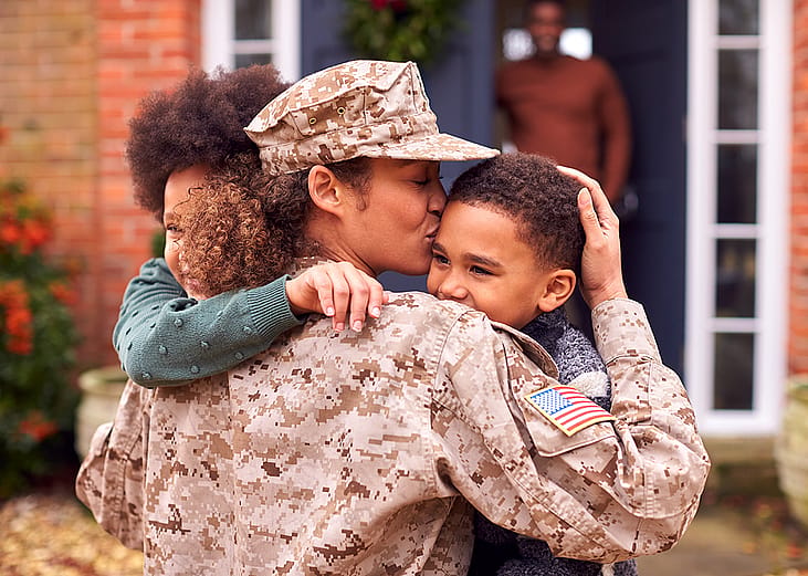 A US female soldier kissing her kids in front of their home after returning.