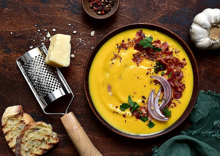 A bowl of autumn pumpkin soup with smoked bacon and grated cheese.