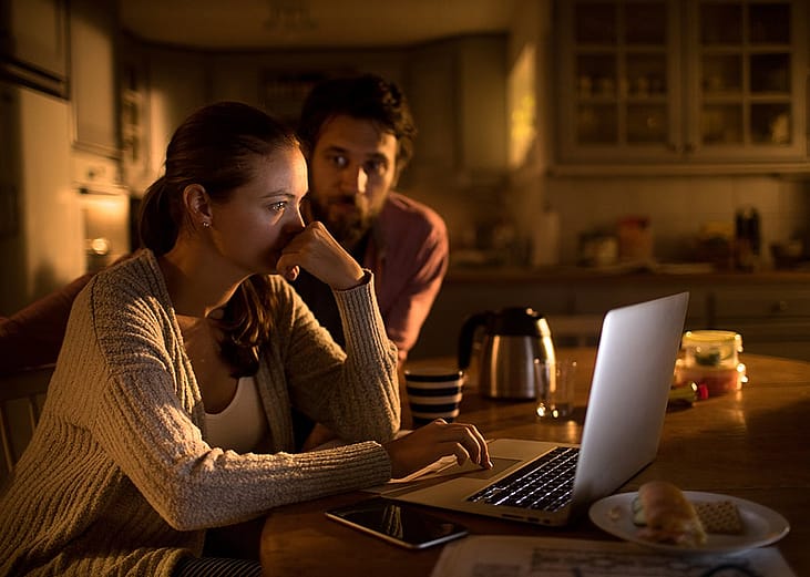 A couple going over their bills and payments on a laptop at their home kitchen.