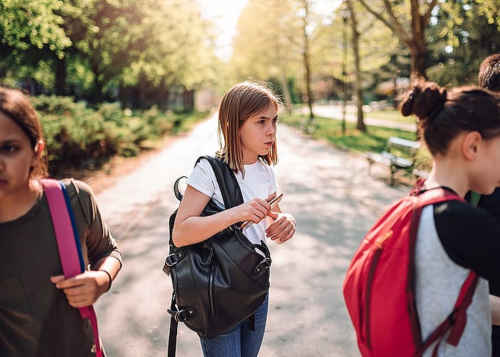 A confused young girl standing alone in a schoolyard among a group of other students.