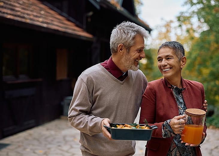 A happy mature couple talking while bringing food and drinks out to the patio.
