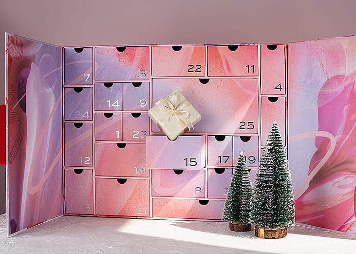 A large pink advent calendar box with small figures of Christmas trees.