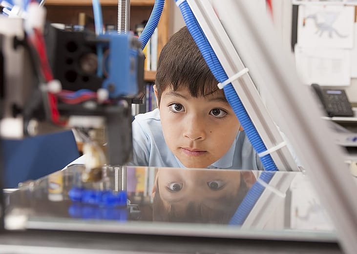 A young boy intently watching his 3D printer finish a project.