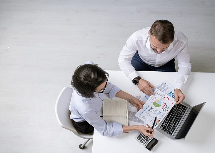 Overhead view of two successful colleagues discussing financial papers with diagrams and charts at a work meeting.