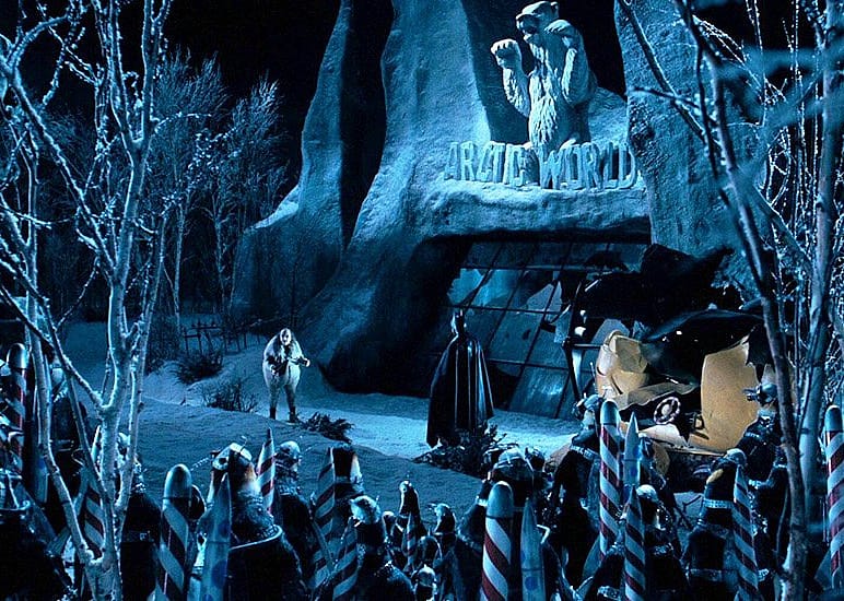 Penguin and Batman stand outside an arctic cave lined with red and white striped poles.