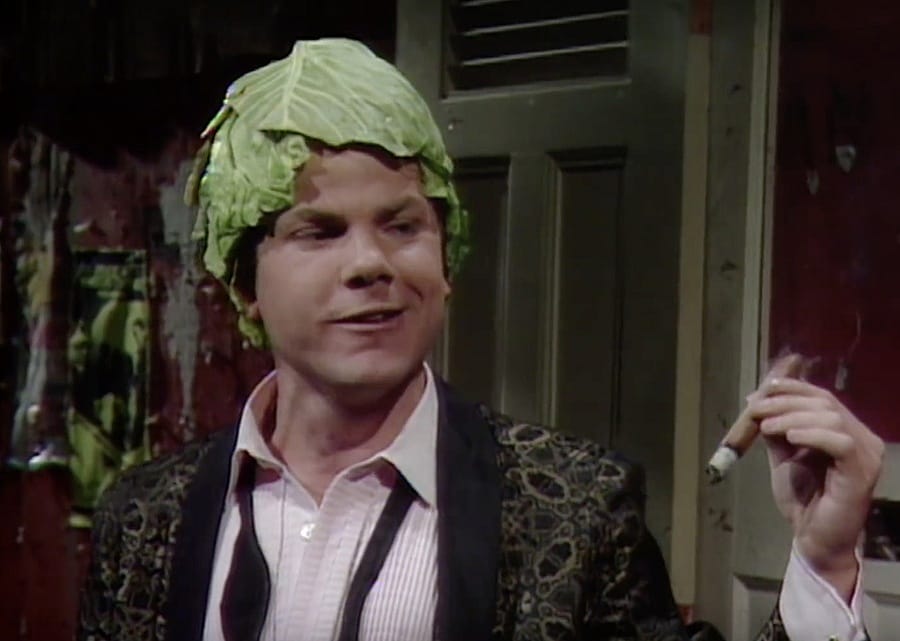 A man smoking a cigar with a cabbage on his head.