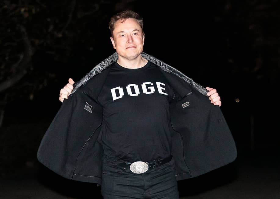 Elon Musk reveals a DOGE t-shirt and a Tesla belt buckle before entering the White House on March 9, 2025. — Joshua Sukoff // Shutterstock.