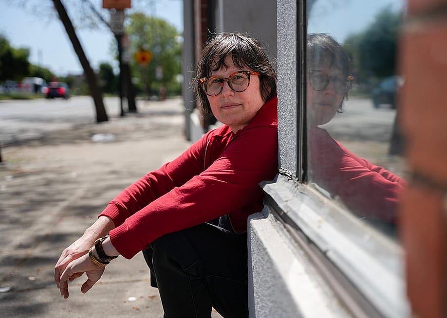 Julie Crossman sitting on a stoop wearing a red long-sleeve shirt, is the sister of Nanie Crossman who she lost touch with, in Oakland on April 8, 2025 — Florence Middleton for CalMatters