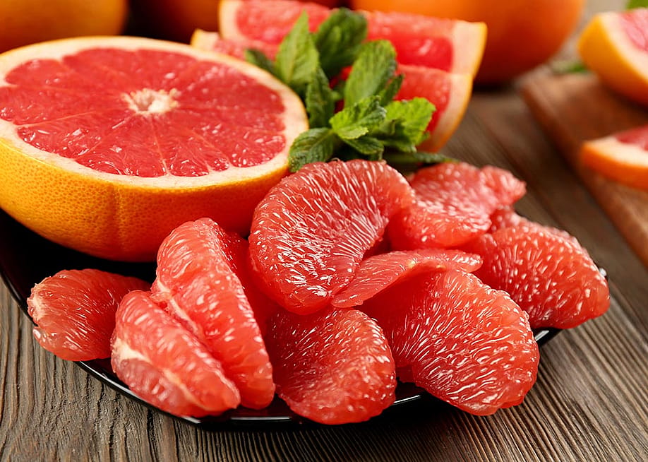 Beauty photo of sliced half a grapefruit on a black plate with peeled pieces of grapefruit in the foreground. — Africa Studio // Shutterstock
