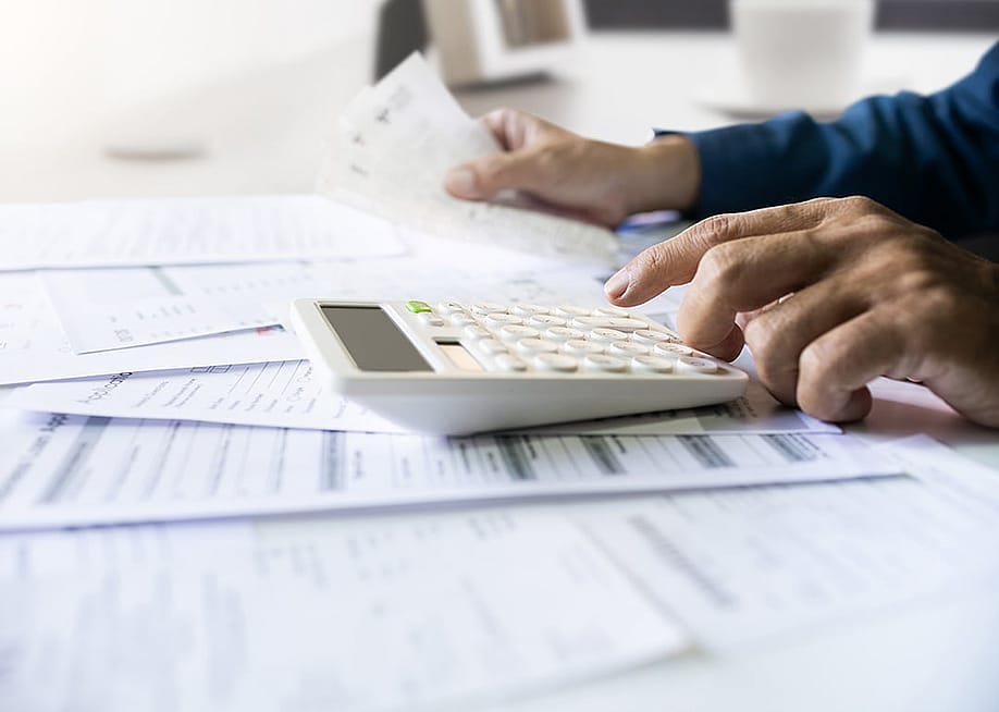 Man calculating figures from paper bills of expenses and other finance documents. — Lek_charoen // Shutterstock