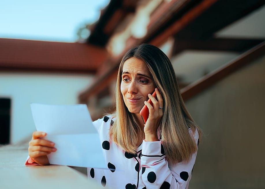 An emotional woman looking at her credit card bill while on the phone. — Nicoleta Ionescu // Shutterstock