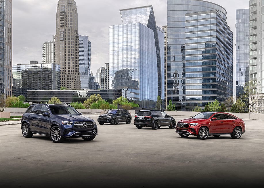 Four models in blue, black and red of the 2024 Mercedes-Benz GLE Coup parked on a rooftop with skyscrapers in the background. — Mercedes