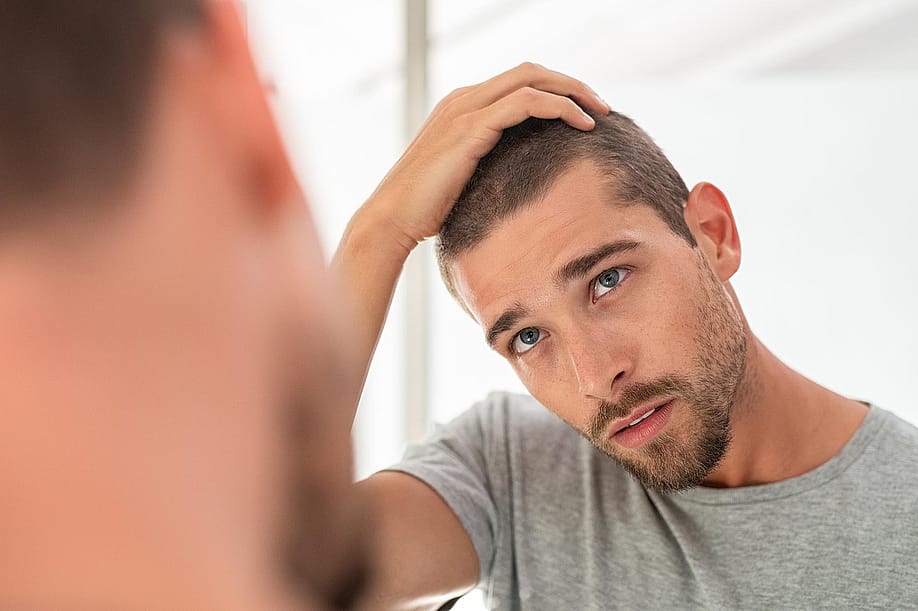 Young man with shaved head looking at mirror in bathroom at home, running fingers over hair.. — Ground Picture // Shutterstock