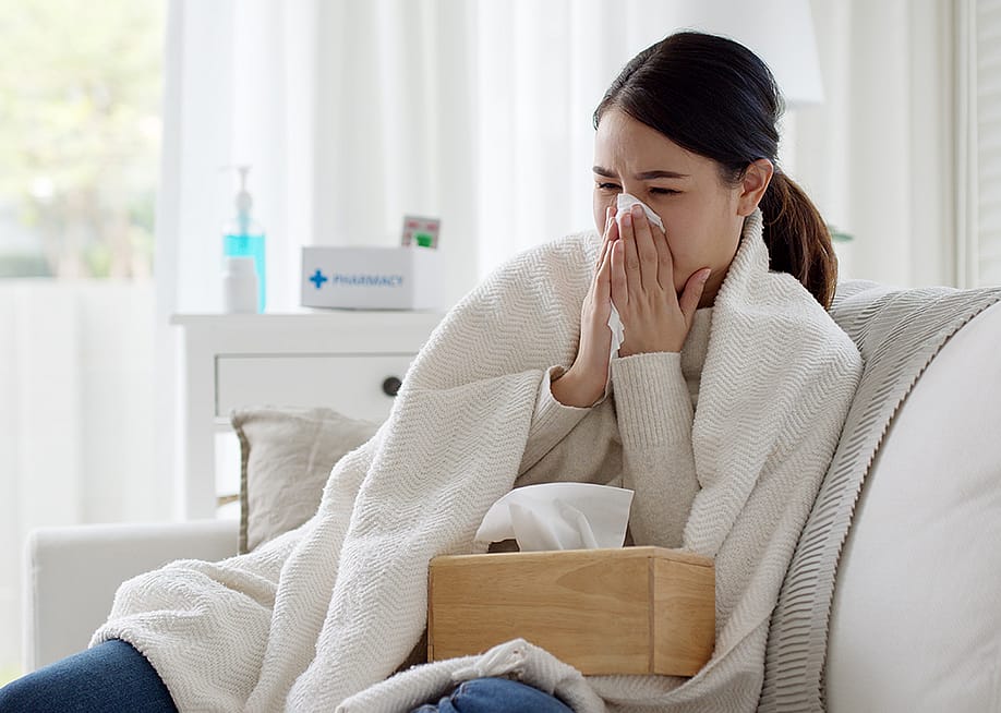 Young woman with a cold sitting under a blanket on a sofa. — Chay_Tee // Shutterstock