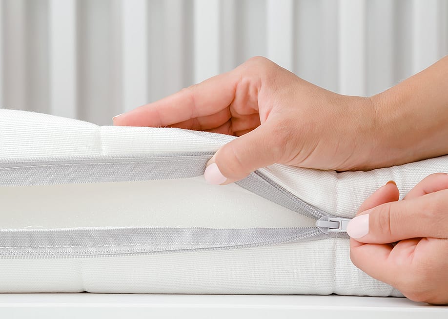 A woman's hand opening the cover of new white mattress to check the quality of a baby's bed. — FotoDuets // Shutterstock