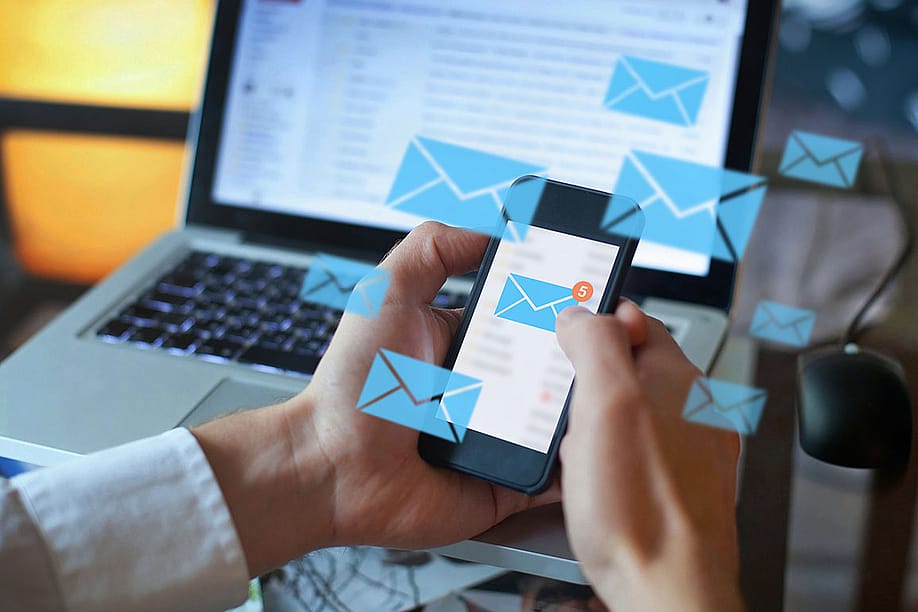 Person holding smartphone with lots of message alert icons superimposed on the screen, with laptop in the background. — Song_about_summer // Shutterstock